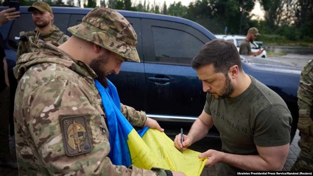 乌克兰总统在访问了顿涅茨克地区前线附近阵地后在一处加油站为一名军人在乌克兰国旗上签名。(2023年6月26日)(photo:VOA)