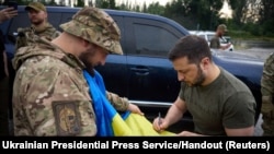 Президент Украины Владимир Зеленский подписывает национальный флаг военнослужащему на заправочной станции после посещения позиций у линии фронта в Донецкой области, 26 июня 2023 года