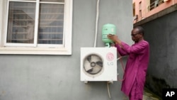 A technician positions an R-22 refrigerant on an outdoor air conditioning unit in Lagos, Nigeria, Thursday, July 18, 2024. (AP Photo/Sunday Alamba)