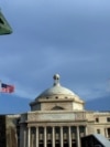 FILE - A bronze statue of San Juan Bautista stands in front the Capitol building flanked by US and Puerto Rican flags, in San Juan, Puerto Rico. 