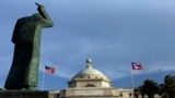 FILE - A bronze statue of San Juan Bautista stands in front the Capitol flanked by U.S. and Puerto Rican flags in San Juan, Puerto Rico. 