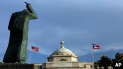 FILE - A bronze statue of San Juan Bautista stands in front the Capitol flanked by U.S. and Puerto Rican flags in San Juan, Puerto Rico. 