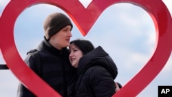 Mariia Vyhivska, from Ukraine, left, and Iurii Kurochkin, from Russia, pose with a heart-shaped sign on the banks of the Ada Ciganlija Lake, in Belgrade, Serbia, Sunday, Feb. 5, 2023. (AP Photo/Darko Vojinovic)