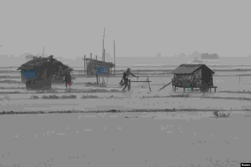 People walk along shrimp and crab farms that are flooded due to heavy rain as Cyclone Remal passes the country, in the Shyamnagar area of Satkhira, Bangladesh.