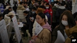 FILE - Chinese job seekers hold brochures to look for job openings at a job fair in Beijing on February 23, 2024.