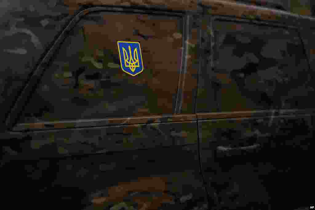 Una pegatina con el escudo de armas de Ucrania, pegado en un auto pintado de camuflaje, en Kiev, Ucrania, el 11 de marzo de 2023. Hay sacos de arena protegiendo estatuas y barreras antitaque en las calles, trincheras en los bosques cercanos y avisos de minas terrestres en el monte. Las señales pintadas en las paredes indican el refugio más próximo, mientras las sirenas antiaéreas suenan ocasionalmente en la ciudad, que a veces sufre ataques con misiles.