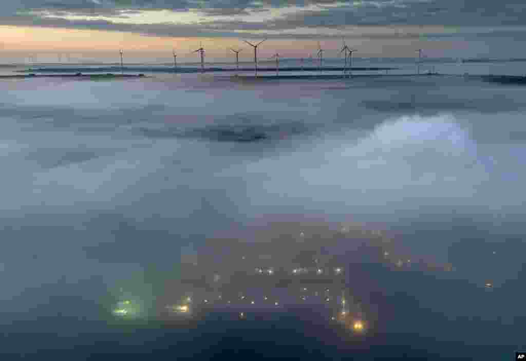 Fog floats over a wind energy plant near Stetten, some 20 kilometres north of Kaiserslautern, Germany, as the sun rises.