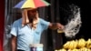 A vendor with an umbrella over his head throws water over the bananas on a hot summer day in Varanasi on May 27, 2024. 