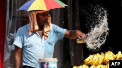 A vendor with an umbrella over his head throws water over the bananas on a hot summer day in Varanasi on May 27, 2024. 