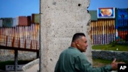 Thomas Correa, of Northern California, talks as he stands in front of a remnant of the Berlin Wall, which sits near the wall that separates the United States from Mexico, in Tijuana, Mexico, Aug. 25, 2023.