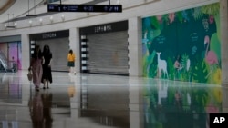 FILE - Women walk past shuttered and vacant shops at a shopping mall in Beijing on July 27, 2023.
