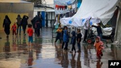 Anak-anak Palestina bermain di tengah hujan di kamp pengungsi di Rafah, di Jalur Gaza selatan, tempat sebagian besar warga sipil mengungsi saat pertempuran antara Israel dan Hamas, 12 Desember 2023. (Foto: AFP)