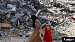 FILE - A woman and child walk among debris, aftermath of Israeli strikes at the area, where Israeli hostages were rescued on Saturday, in Nuseirat refugee camp in the central Gaza Strip, June 9, 2024.