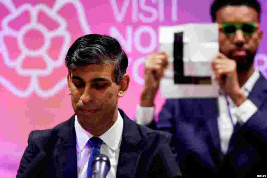 Independent candidate Niko Omilana holds an "L" sign behind British Prime Minister Rishi Sunak as he speaks after winning his seat at Richmond and Northallerton during the UK election in Northallerton, Britain.