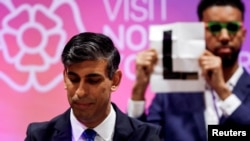 Independent candidate Niko Omilana holds an "L" sign behind British Prime Minister Rishi Sunak as he speaks after winning his seat at Richmond and Northallerton during the UK election in Northallerton, Britain.