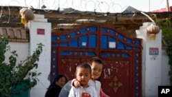 FILE - Uyghur youths play outside their house, with Chinese lanterns and barbed wire visible, at Unity New Village in Hotan, China, Sept 20, 2018. Xinjiang authorities have been replacing names of ethnic minorities' villages to reflect Communist ideology.