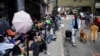 FILE - Migrants sit in a queue outside the Roosevelt Hotel, which is being used by the city as temporary housing, on July 31, 2023, in New York. New York mayor calls for changes in city’s migrant sanctuary status.