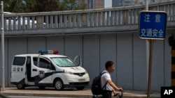 A man pushes a bicycle past by a police van stationed at a bridge along the Chang'an Avenue in Beijing, June 4, 2024. 