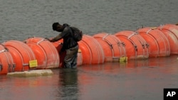 A migrant from Colombia stands at a floating buoy barrier as he looks to cross the Rio Grande from Mexico into the US, Aug. 21, 2023, in Eagle Pass, Texas. 