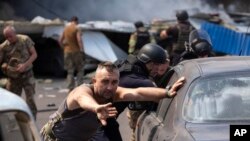 Trabajadores de emergencia y soldados empujan automóviles dañados después de que un misil ruso impactara un supermercado en Kostiantynivka, Ucrania, el 9 de agosto de 2024.