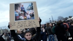 A woman holds a placard depicting French President Emmanuel Macron sitting on garbage cans that reads, 'king of trash' during a protest in Paris, Friday, March 17, 2023.