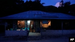 Bara Kilimandang stands at the door of his house whose electricity comes from solar energy in Walatungga on Sumba Island, Indonesia, Tuesday, March 21, 2023. (AP Photo/Dita Alangkara)