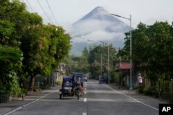 Seorang perempuan mengendarai sepeda roda tiga dengan latar belakang gunung berapi Mayon terlihat dari Legazpi, provinsi Albay, Filipina timur laut, Selasa, 13 Juni 2023. (AP/Aaron Favila)