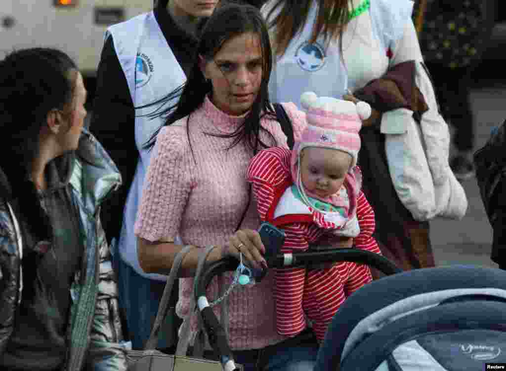 Una mujer carga a un niño mientras civiles evacuados llegan a una estación de ferrocarril local, después de que funcionarios instalados en Rusia ampliaran una orden de evacuación a la zona a lo largo de la orilla oriental del río Dnipro, el 2 de noviembre de 2022.&nbsp;