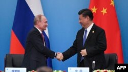 ARCHIVES - Le président chinois Xi Jinping (à droite) serre la main de son homologue russe Vladimir Poutine dans la province chinoise du Shandong, le 10 juin 2018.