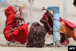 Women quench their thirst with tap water on a hot summer afternoon during a heat wave in Prayagraj, India on June 10, 2024. (Photo by Anil SHAKYA / AFP)