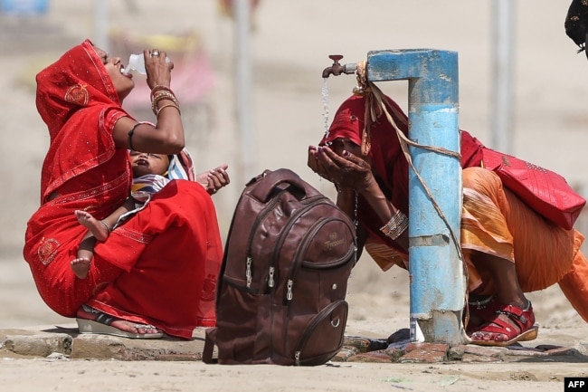 Women quench their thirst with tap water on a hot summer afternoon during a heat wave in Prayagraj, India on June 10, 2024. (Photo by Anil SHAKYA / AFP)