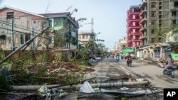Locals ride motorbike while lamp-posts and trees are fallen after Cyclone Mocha in Sittwe township, Rakhine State, Myanmar, Monday, May 15, 2023.