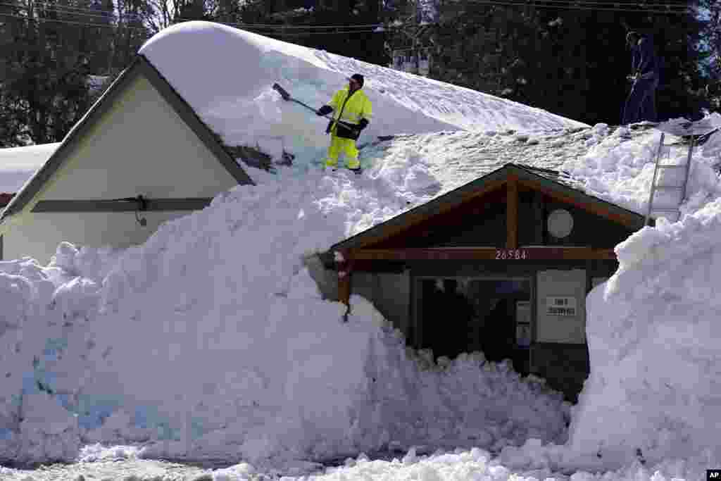 A worker clears snow off the roof of Skyforest Elks Lodge after a series of storms, March 8, 2023, in Rimforest, California.