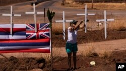 Sunya Schlea ties roses to crosses along the Lahaina Bypass in Lahaina, Hawaii, Aug. 22, 2023, to honor the victims killed in a wildfire.