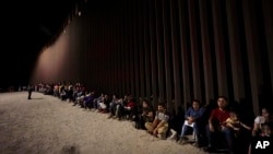 FILE - Migrants wait along a border wall Aug. 23, 2022, after crossing from Mexico near Yuma, Ariz.
