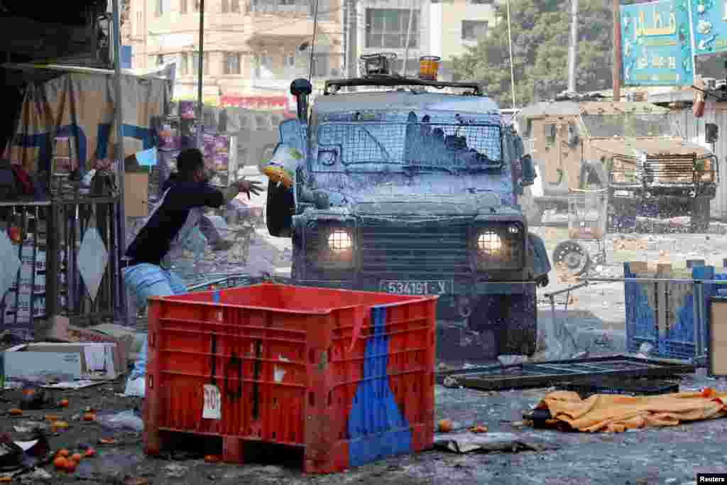 A Palestinian hurls a paint bucket at an Israeli military vehicle during a raid in Nablus in the Israeli-occupied West bank.