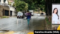 Una mujer camina en una calle de Caracas resguardada de la lluvia bajo un paraguas, el martes 30 de mayo de 2023.