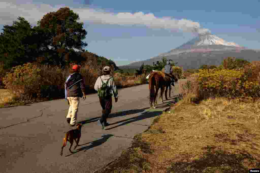 Residentes caminan a lo largo de una vía mientras el humo y las cenizas emergen del volcán Popocatépetl, luego de un aumento en la actividad volcánica, visto desde la ciudad de Santiago Xalizintla, México.