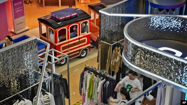 FILE - Women and their children ride on a miniature train passing shoppers at a mall in Beijing, Aug. 20, 2023. Chinese leader Xi Jinping recently called for patience in a speech as the ruling Communist Party tries to reverse a deepening economic slump.