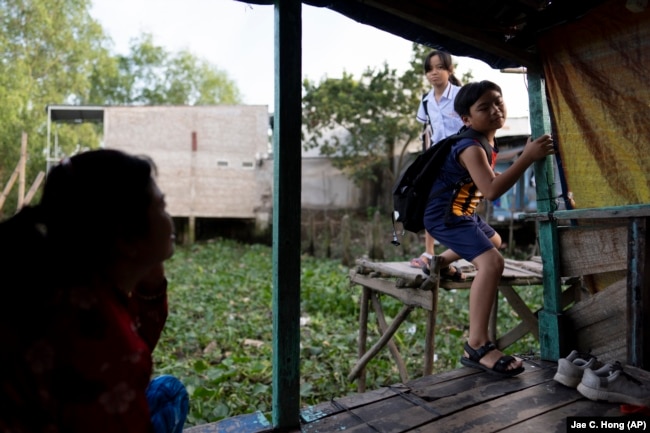 Nguyen Thi Thuy sits on her houseboat as her grandchildren, Do Hoang Trung and his sister, Do Bao Tran, return from school, Jan. 17, 2024. (AP Photo/Jae C. Hong)