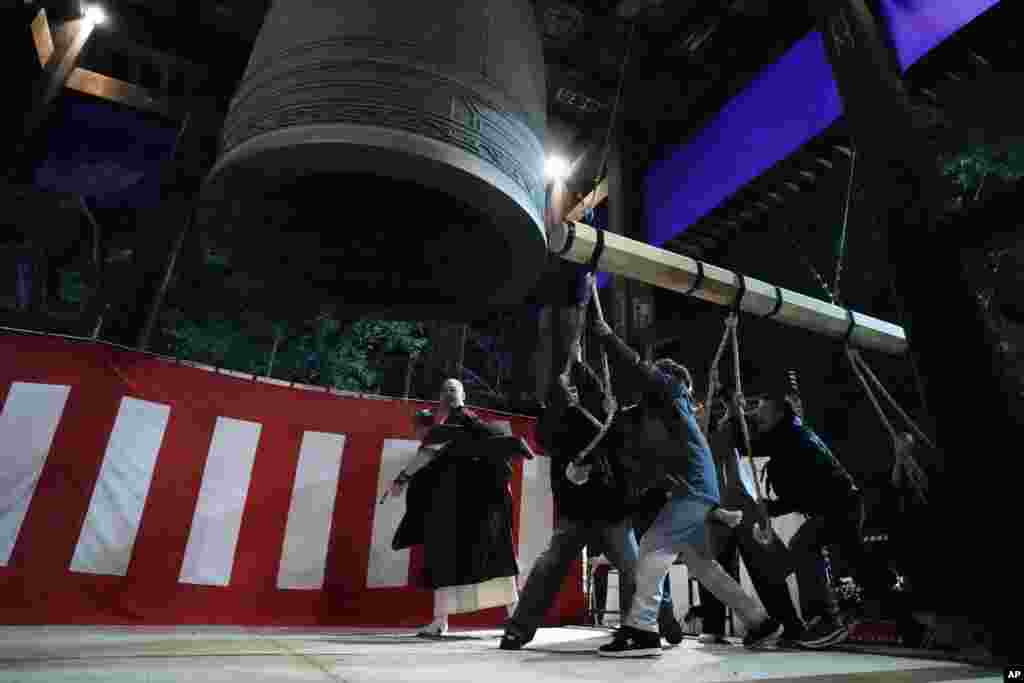 People strike a giant bell to celebrate the New Year at the Zojoji Buddhist temple, minutes after midnight, Jan. 1, 2024, in Tokyo, Japan. 