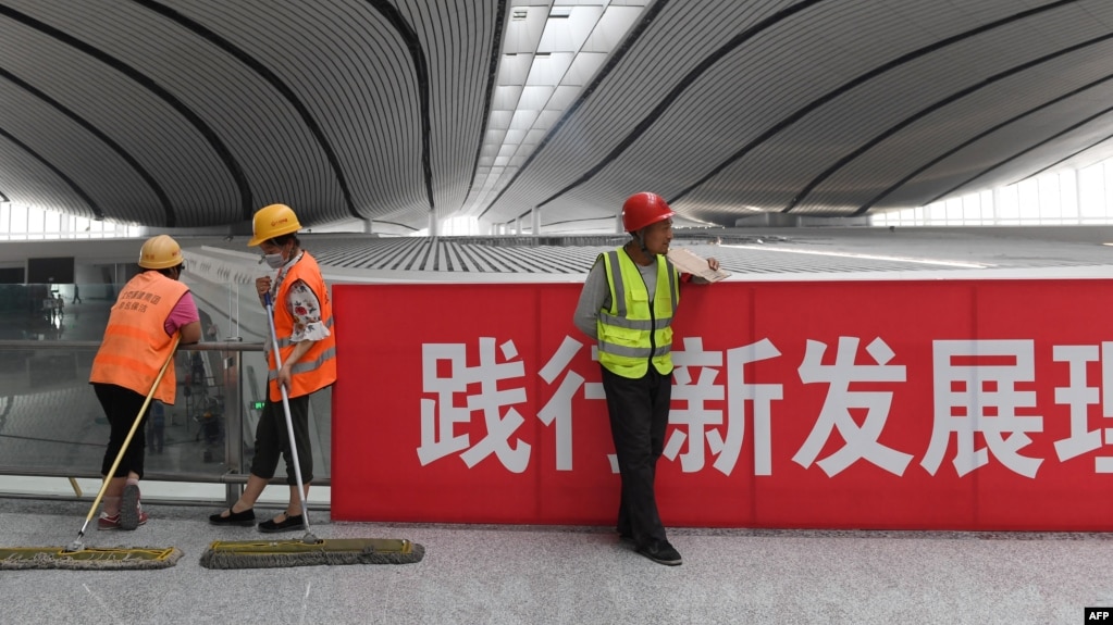 资料照：北京大兴国际机场的工人在一幅“践行新发展理论”的标语旁工作。（2019年7月9日）