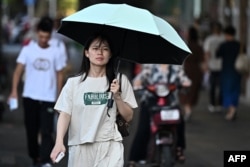 一名女子打着遮阳伞在酷暑中的武汉街头行走。（2024年8月1日）