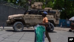 A man carries dry cleaning past an armored police vehicle in Port-au-Prince, Haiti, April 28, 2024.