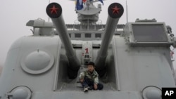 FILE - A child sits near canons on a retired warship at the Chinese People's Liberation Army Naval Museum in Qingdao in eastern China's Shandong province on April 23, 2024.