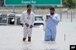 Two men walk through floodwater in Dubai, United Arab Emirates, Wednesday, April 17, 2024. The desert nation attempted to dry out Wednesday from the heaviest rain ever recorded there. (AP Photo/Jon Gambrell)