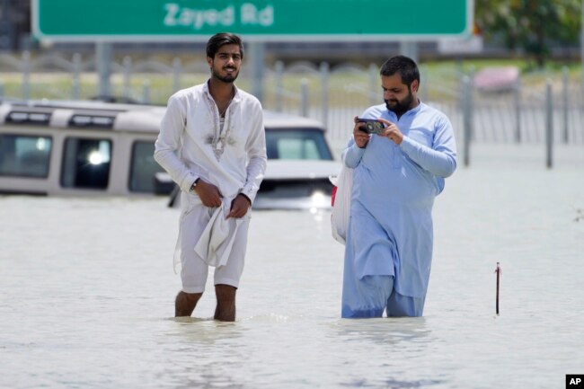 Two men walk through floodwater in Dubai, United Arab Emirates, Wednesday, April 17, 2024. The desert nation attempted to dry out Wednesday from the heaviest rain ever recorded there. (AP Photo/Jon Gambrell)