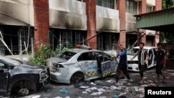 Warga berjalan di samping mobil-mobil yang rusak di Kantor Polisi Mohammadpur, setelah pengunduran diri Perdana Menteri Bangladesh Sheikh Hasina, di Dhaka, Bangladesh, pada 6 Agustus 2024. (Foto: REUTERS/Mohammad Ponir Hossain)