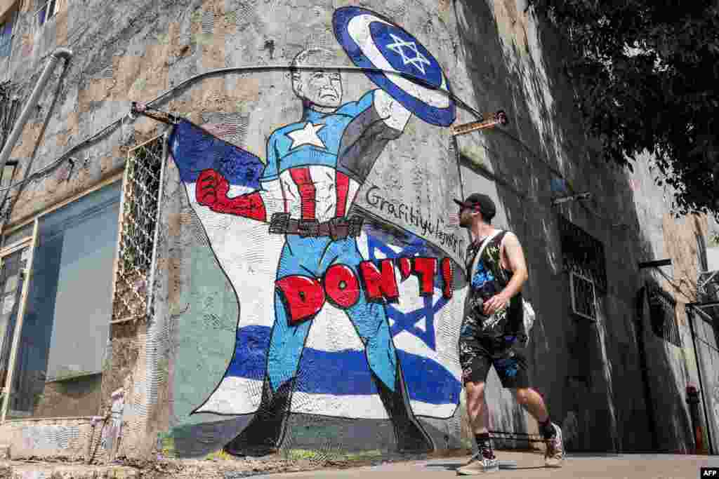 Seorang pria berjalan melewati mural yang digambar oleh kelompok seni grafiti &quot;Grafitiyul&quot; yang menggambarkan Presiden AS Joe Biden berpakaian karakter komik Marvel &quot;Captain America&quot; berdiri di depan bendera Israel dan mengangkat perisainya yang bergambar simbol Bintang Daud, di pinggir jalan kota Tel Aviv. (AFP)&nbsp;