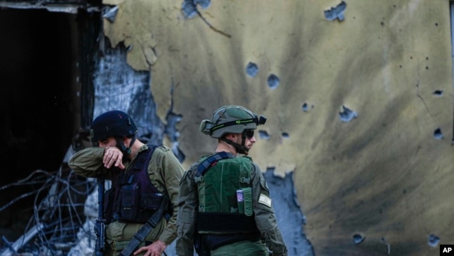 Soldados israelíes pasan junto a casas destruidas por militantes de Hamas en el Kibbutz Be'eri, Israel, el sábado 14 de octubre de 2023.